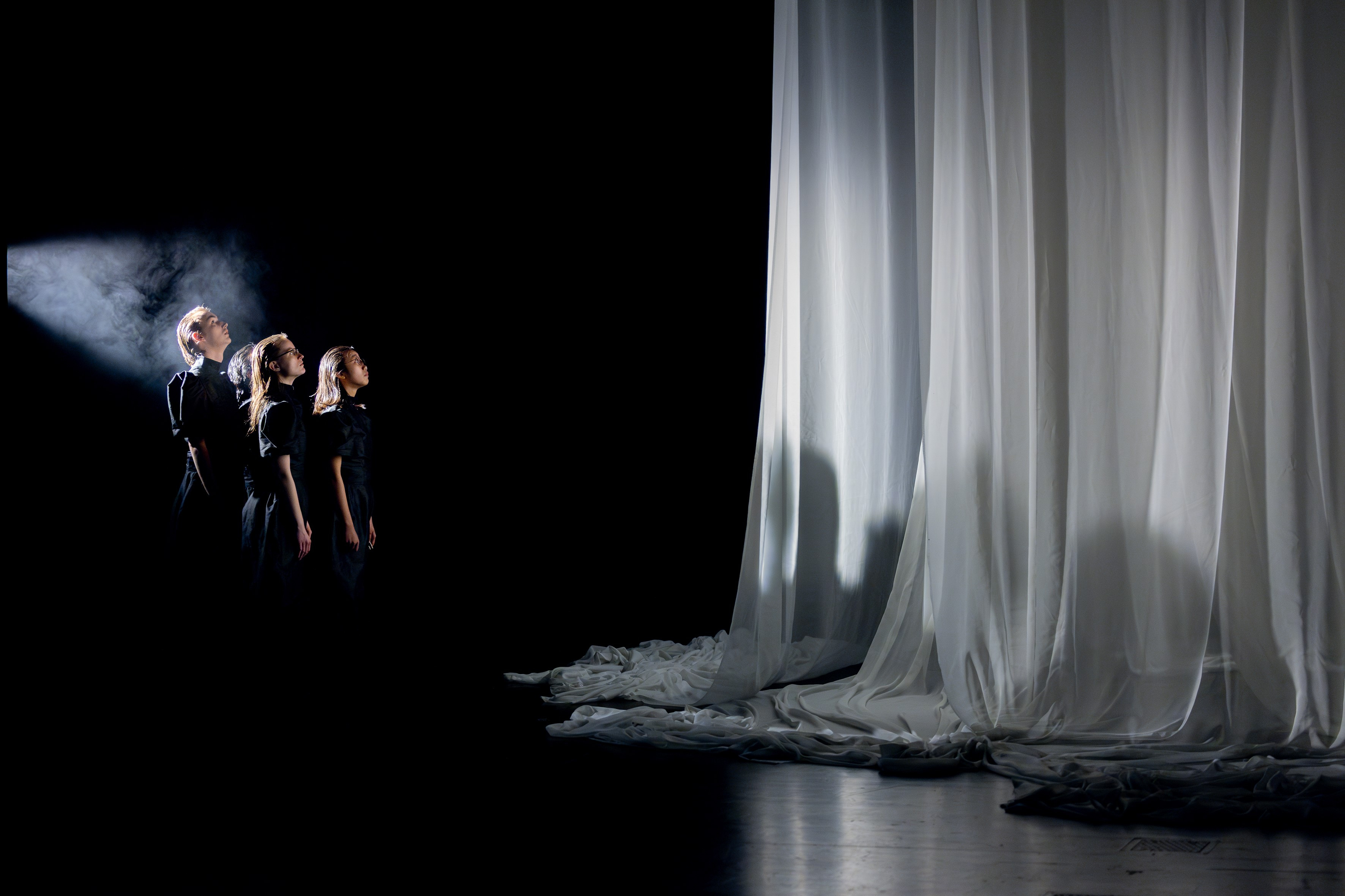 3 people on a black stage with a white curtain