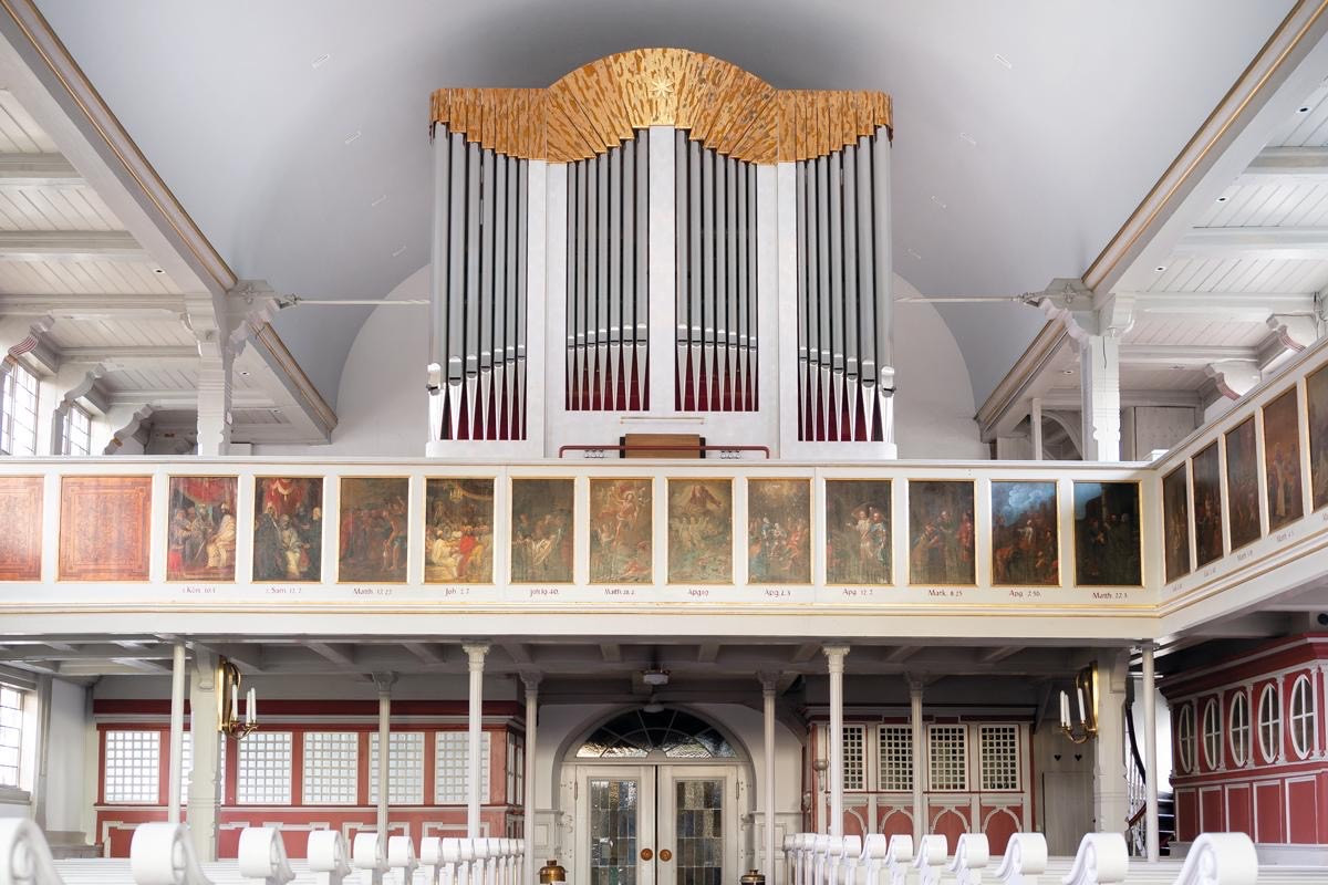 Blick in hellen Kirchenraum mit Sitzreihen und Orgel auf Empore