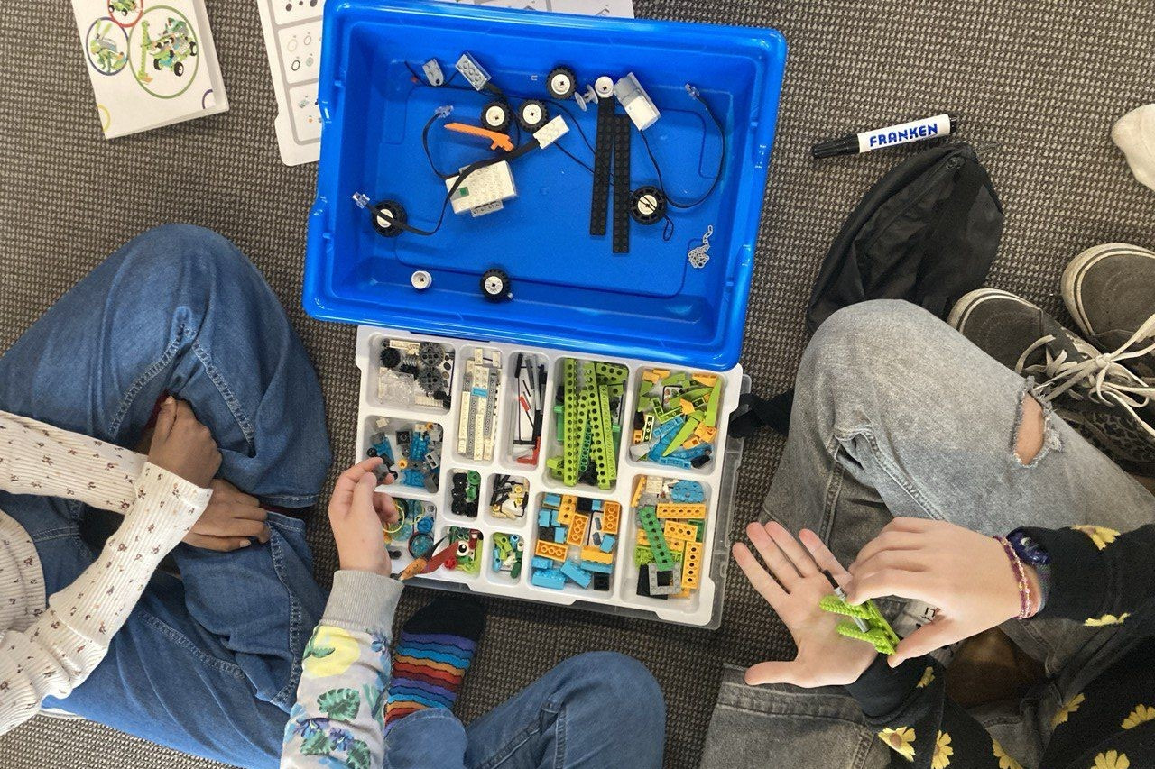 Kiste mit Legosteinen und Kabeln. Reingreifende Kinderhände, von oben
