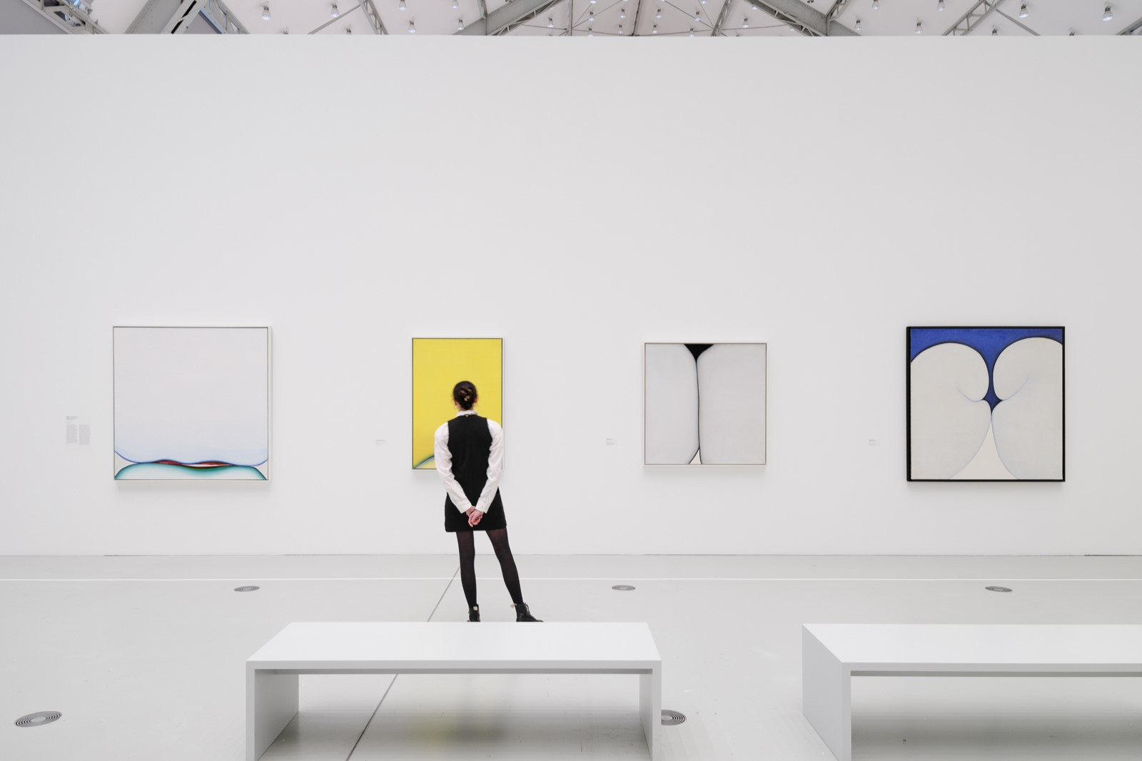 Frau von hinten in einem großen Ausstellungshalle vor 3 Bildern